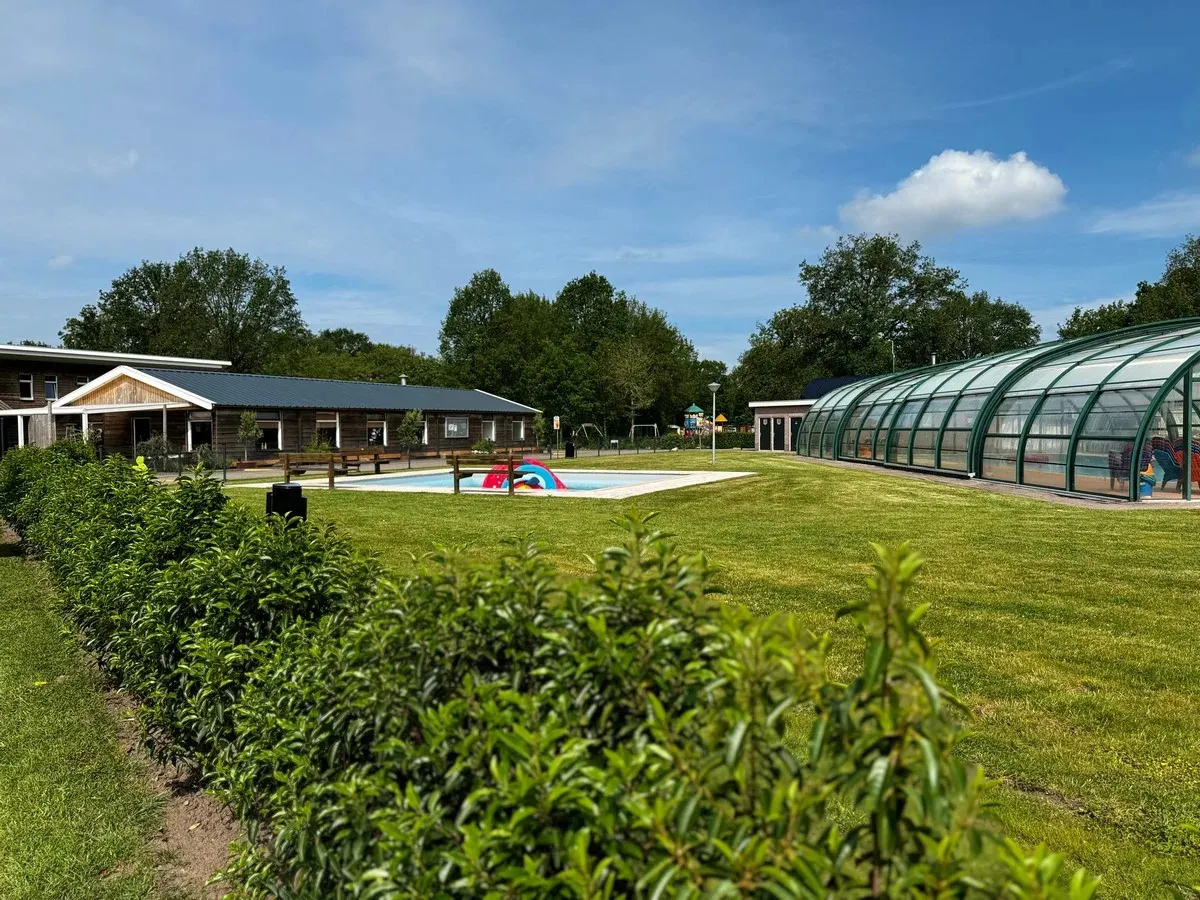 Grasveld met zwembad en een overkapping bij het binnenzwembad op Vakantiepark Mooi Oavelt